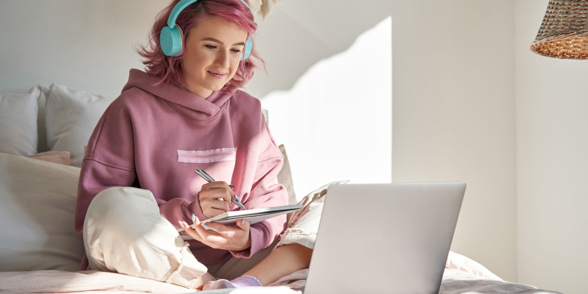 An online coding school allows you to learn from home A woman sits on her bed with her laptop studying at an online coding school.